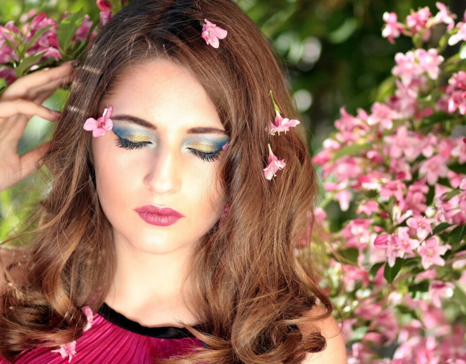 A woman with pink makeup and flowers in her hair and her eyes closed.