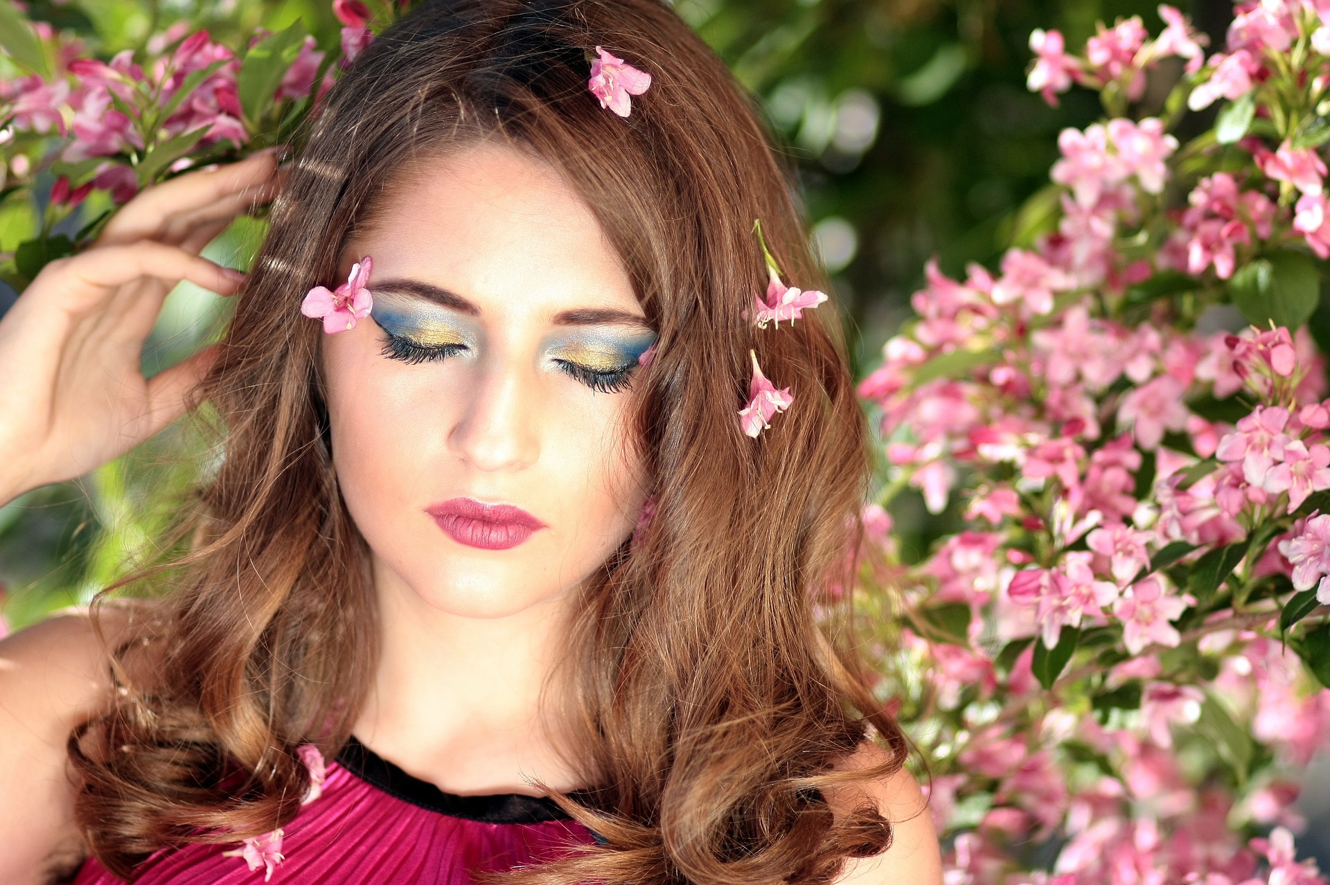 A woman with pink makeup and flowers in her hair and her eyes closed.