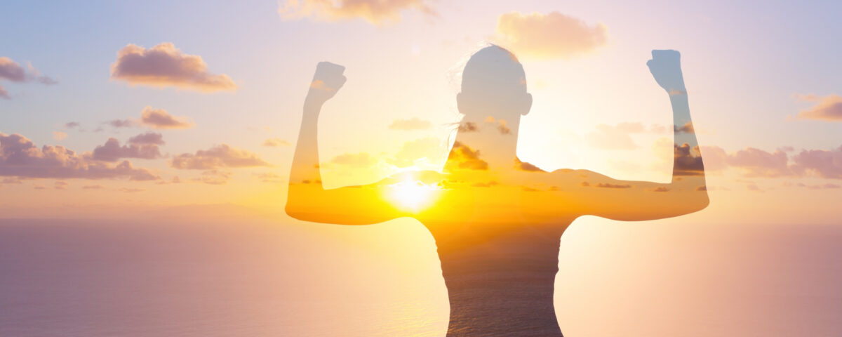 A silhouette of a woman with her arms raised in the air at sunset.