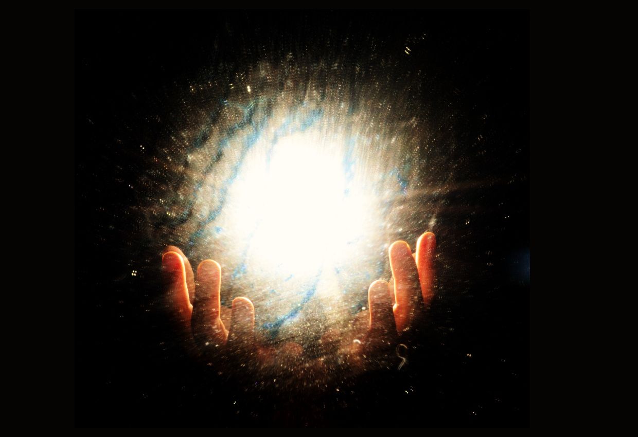 A person's hands are holding a glowing ball of light in the dark.