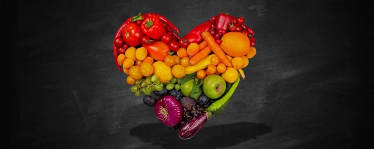 Heart shape created with various fruits and vegetables on a blackboard background