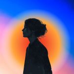 The silhouette of a young woman with an orange color aura on a pink and blue background.
