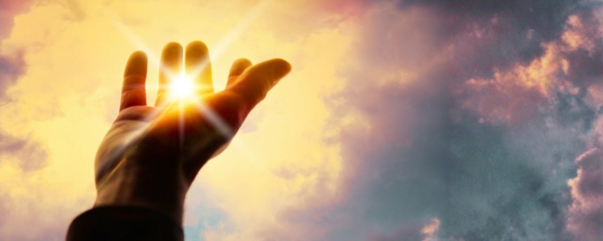 A person extends their hand upward towards the sun, symbolizing the power of blessings and connection with the Divine.