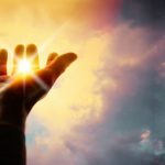 A person extends their hand upward towards the sun, symbolizing the power of blessings and connection with the Divine.