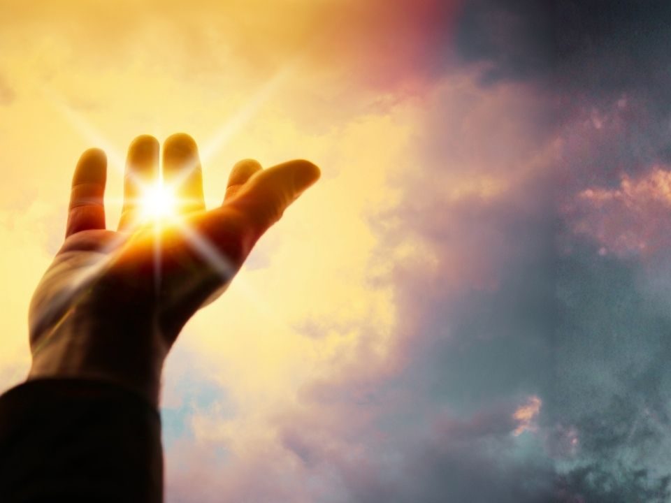 A person extends their hand upward towards the sun, symbolizing the power of blessings and connection with the Divine.
