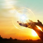 Hands uplifted towards a luminous sun orb, conveying themes of enlightenment and inspiration in a warm atmosphere.