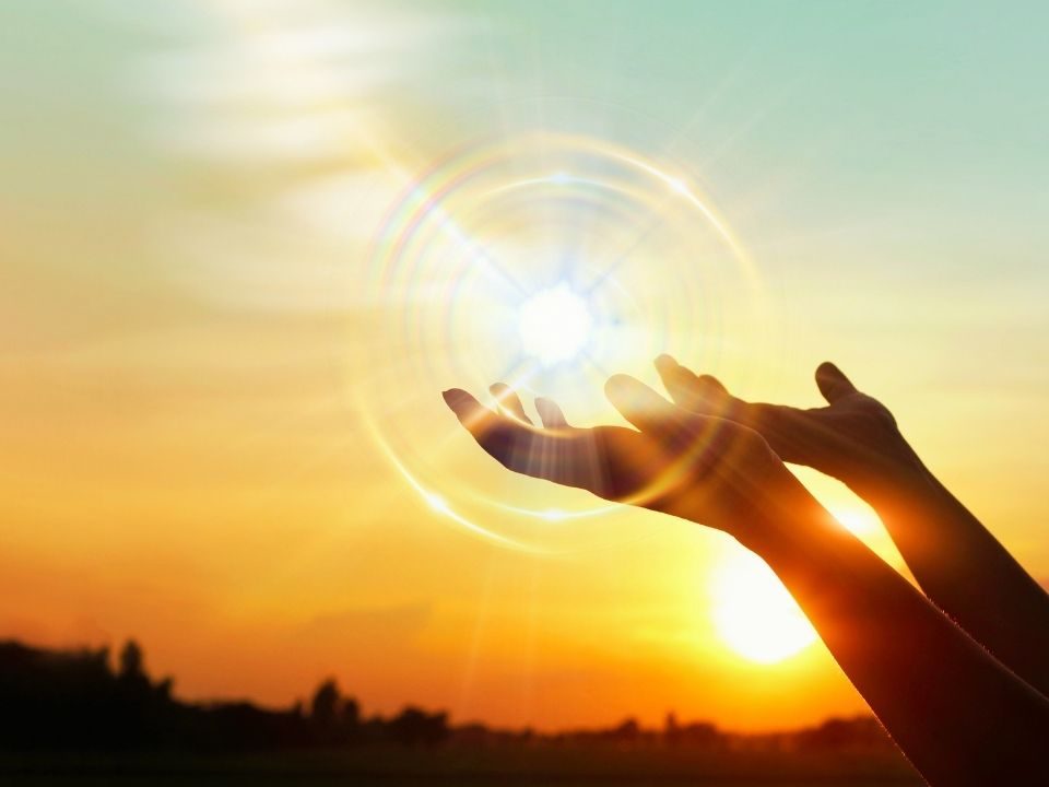 Hands uplifted towards a luminous sun orb, conveying themes of enlightenment and inspiration in a warm atmosphere.